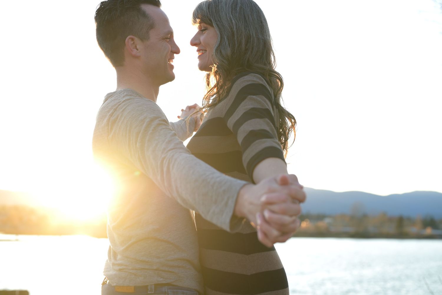 Couple with outstretched arms in front of a sun flare.