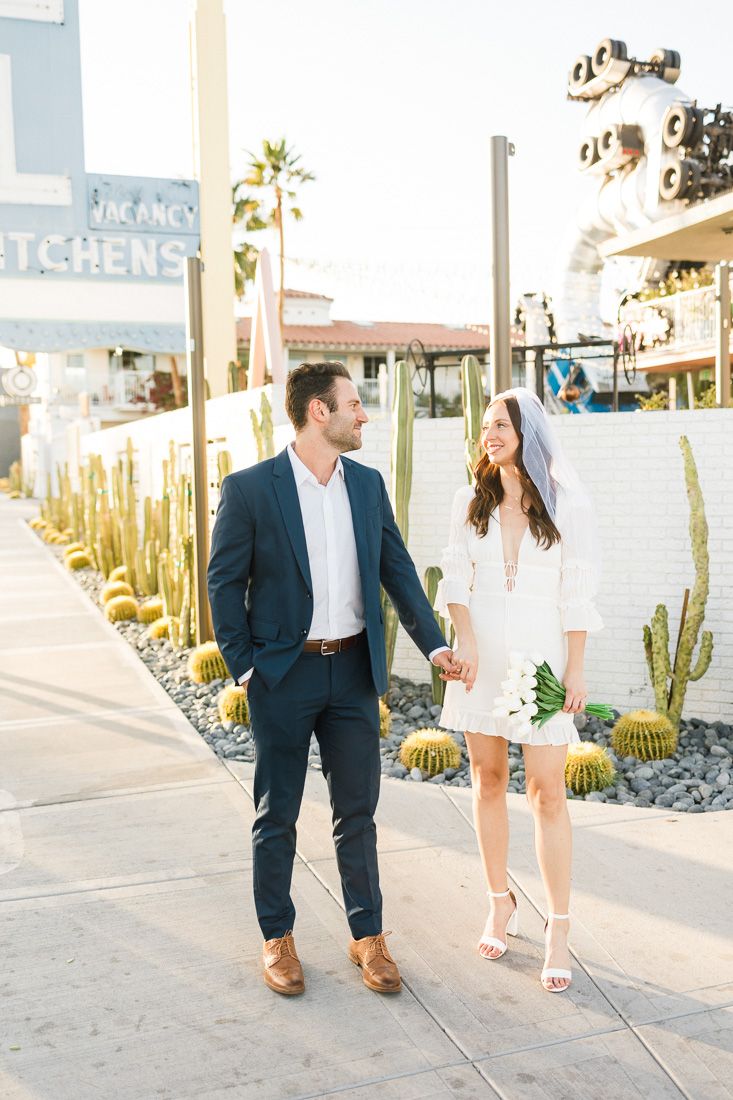 Couple strolling hand in hand past desert landscaping outside a modern restaurant.