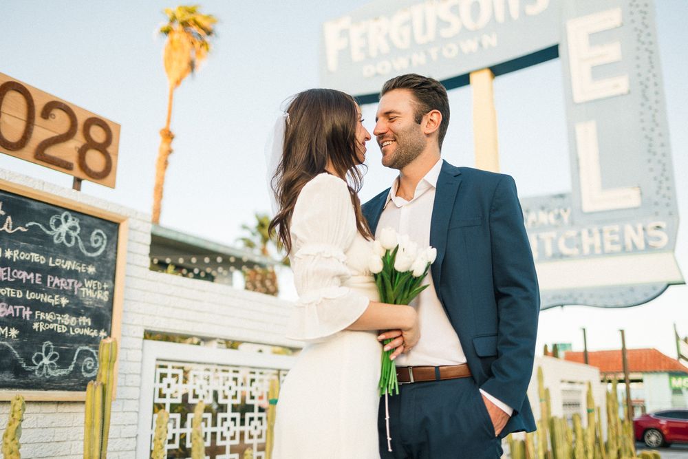 Romantic moment between a couple holding flowers outside a restaurant with palm trees.