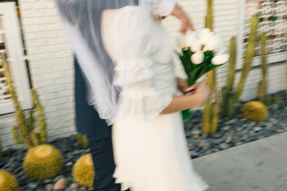 Motion blur photo of couple with white flowers against desert garden backdrop.