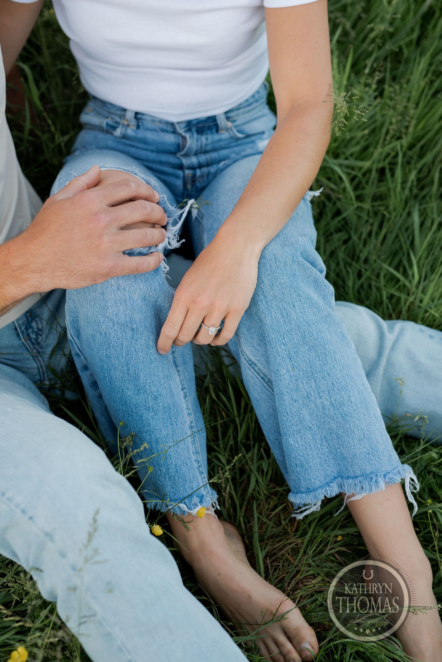 Close-up shot of hands and denim-clad legs sitting in green grass.