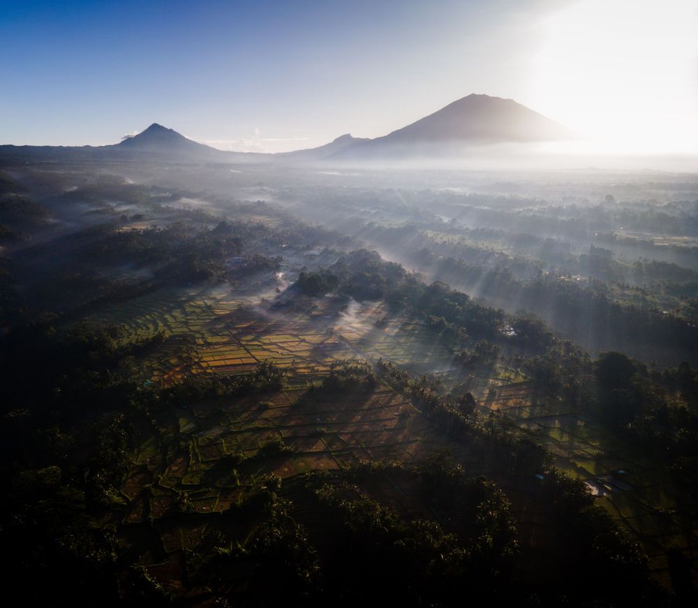 Morning fog rolls through terraced landscape with twin mountain peaks at sunrise.
