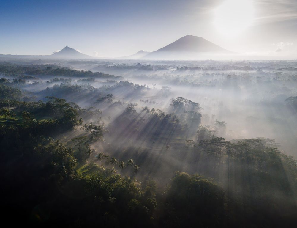 Ethereal morning light rays pierce through fog over mountainous landscape with distant peaks.
