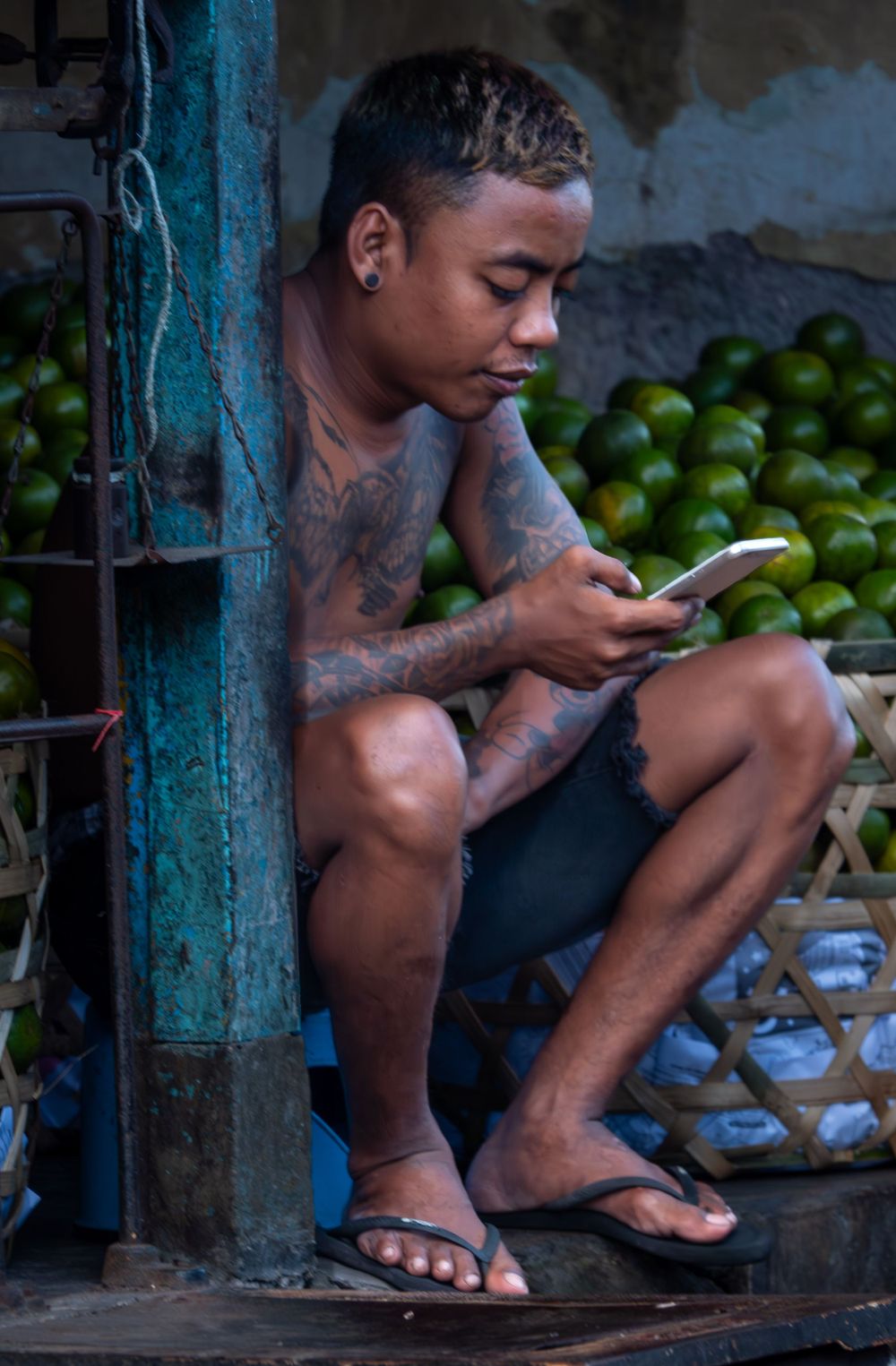 Street vendor checking phone while sitting with fresh limes at a market stall.