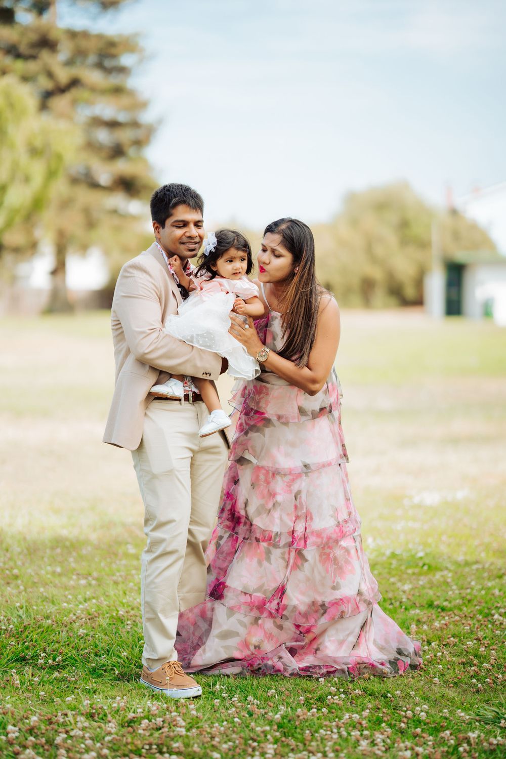 Family in coordinated outfits sharing tender moment together in outdoor park setting.