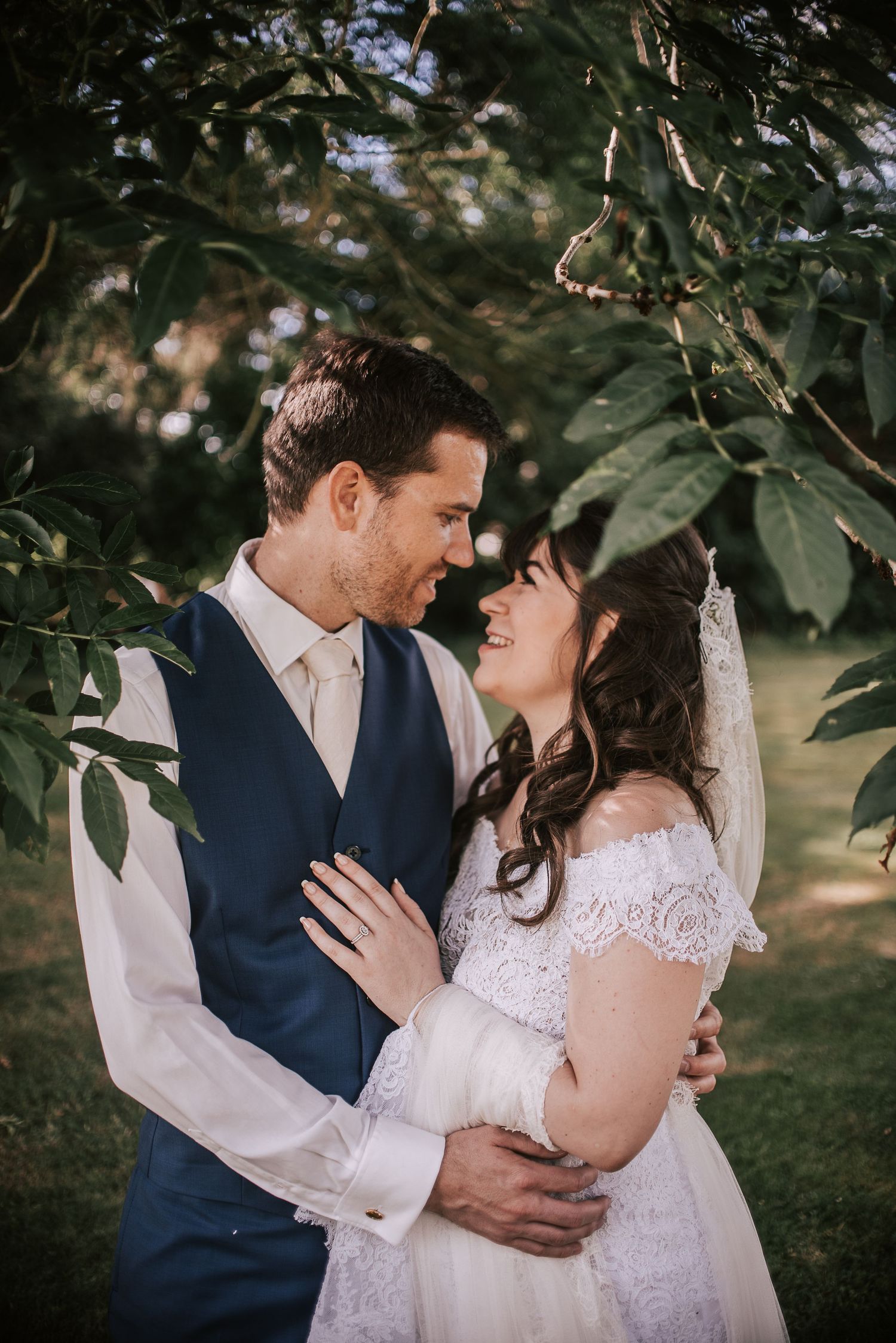 Tender wedding portrait of couple embracing under green foliage.