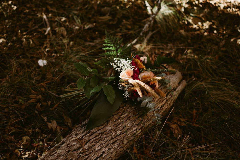 A colorful floral bouquet lies on a fallen tree trunk in a moody forest setting.