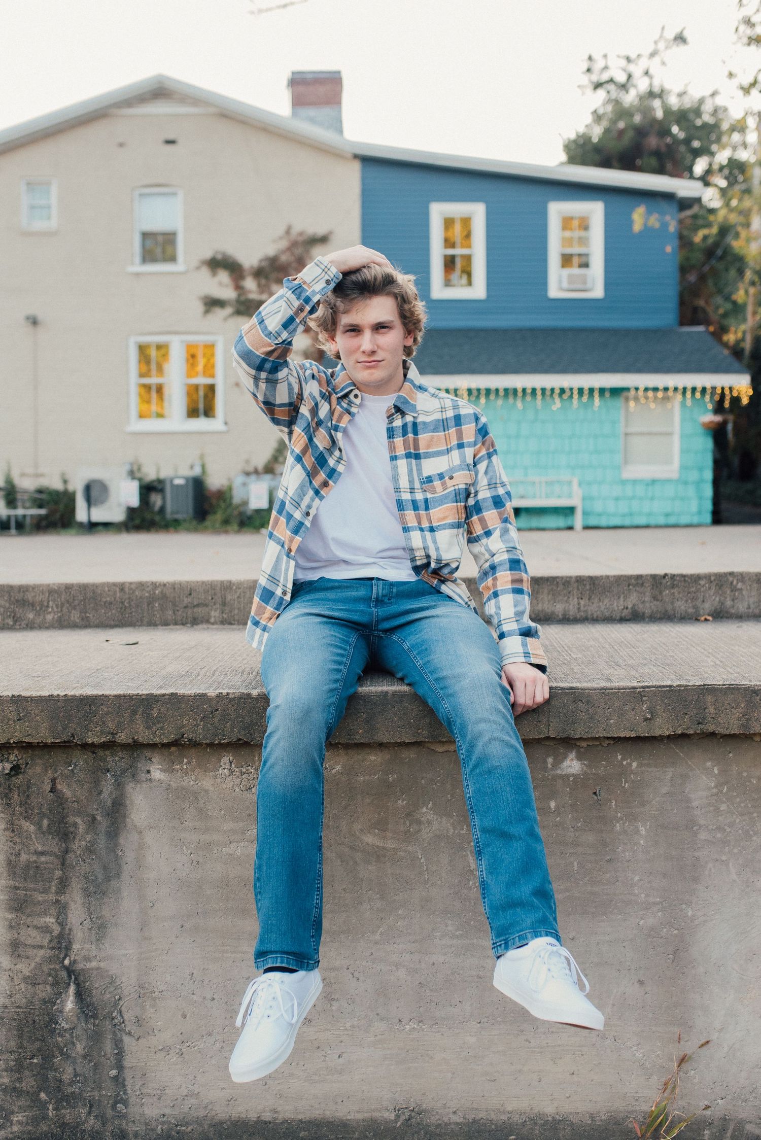 Casual portrait of someone sitting on a concrete wall with colorful houses in the background.