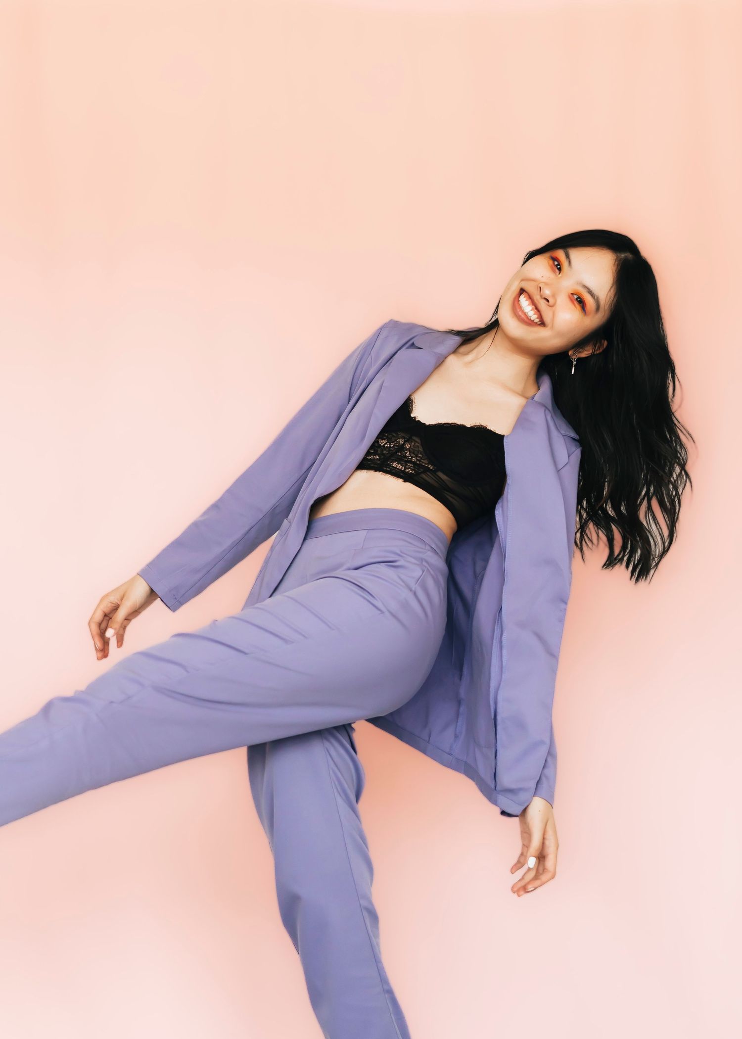 Person in purple suit strikes playful pose against pink background.