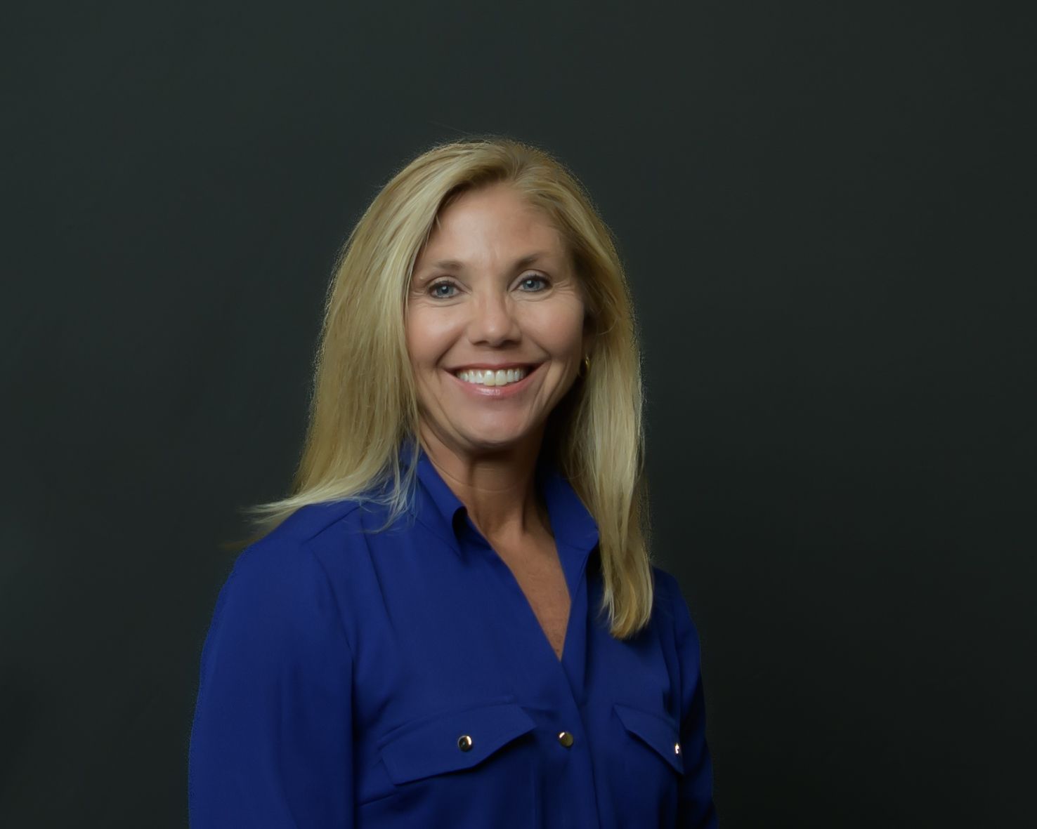 Professional headshot of person in blue button-up blouse against dark background.