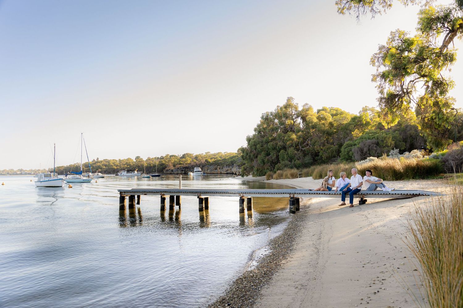 Scenic waterfront pier with boats and people walking along beach at sunset.