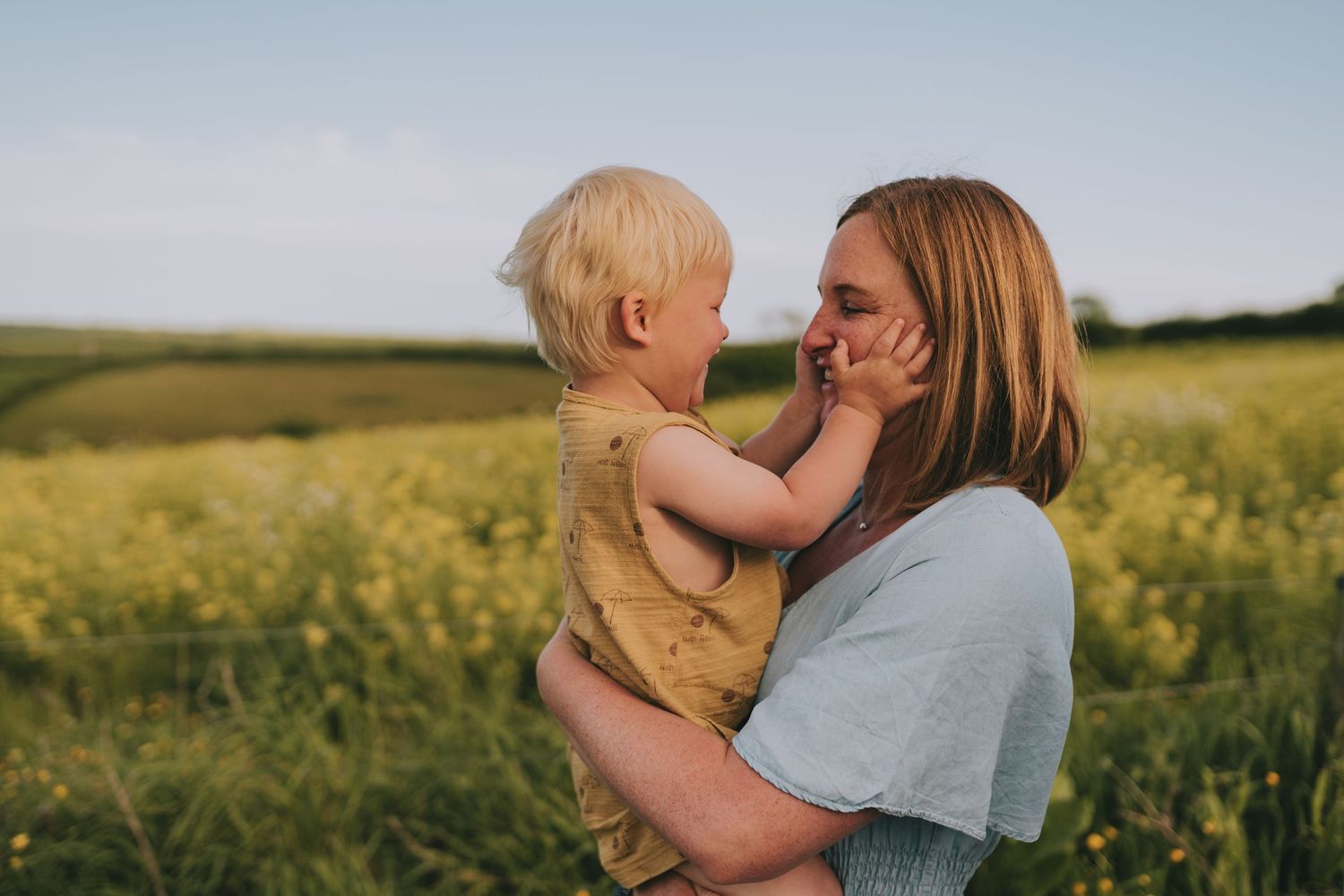 Mother and toddler sharing tender moment in blooming yellow rapeseed field.