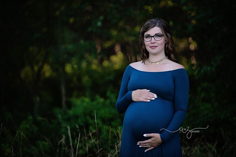 Maternity portrait of someone in navy dress against dark forest background.