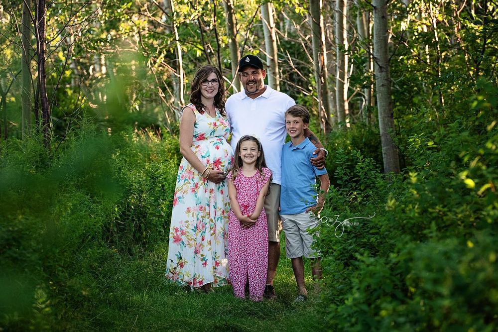 A family portrait taken outdoors in a lush green forest setting.
