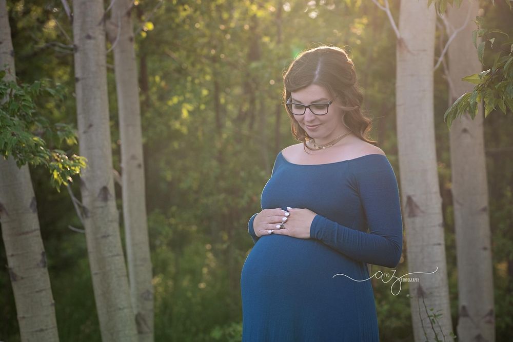 Maternity portrait of someone in a blue dress standing among birch trees.