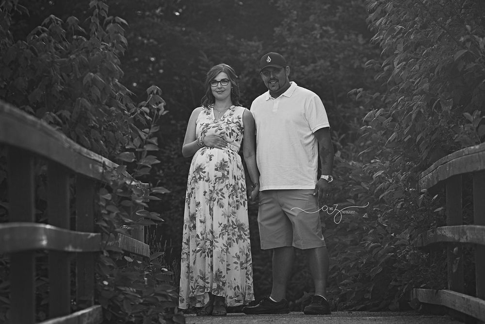 A couple stands together on a wooden bridge in a black and white photograph.