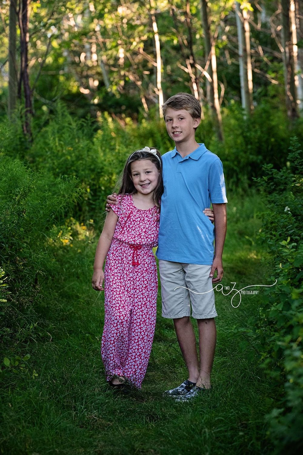 A young pair posing together on a wooded path wearing blue and pink summer outfits.