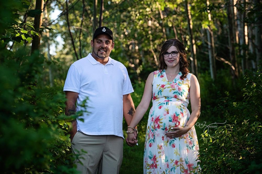 A couple poses together in a garden setting during maternity photography session.