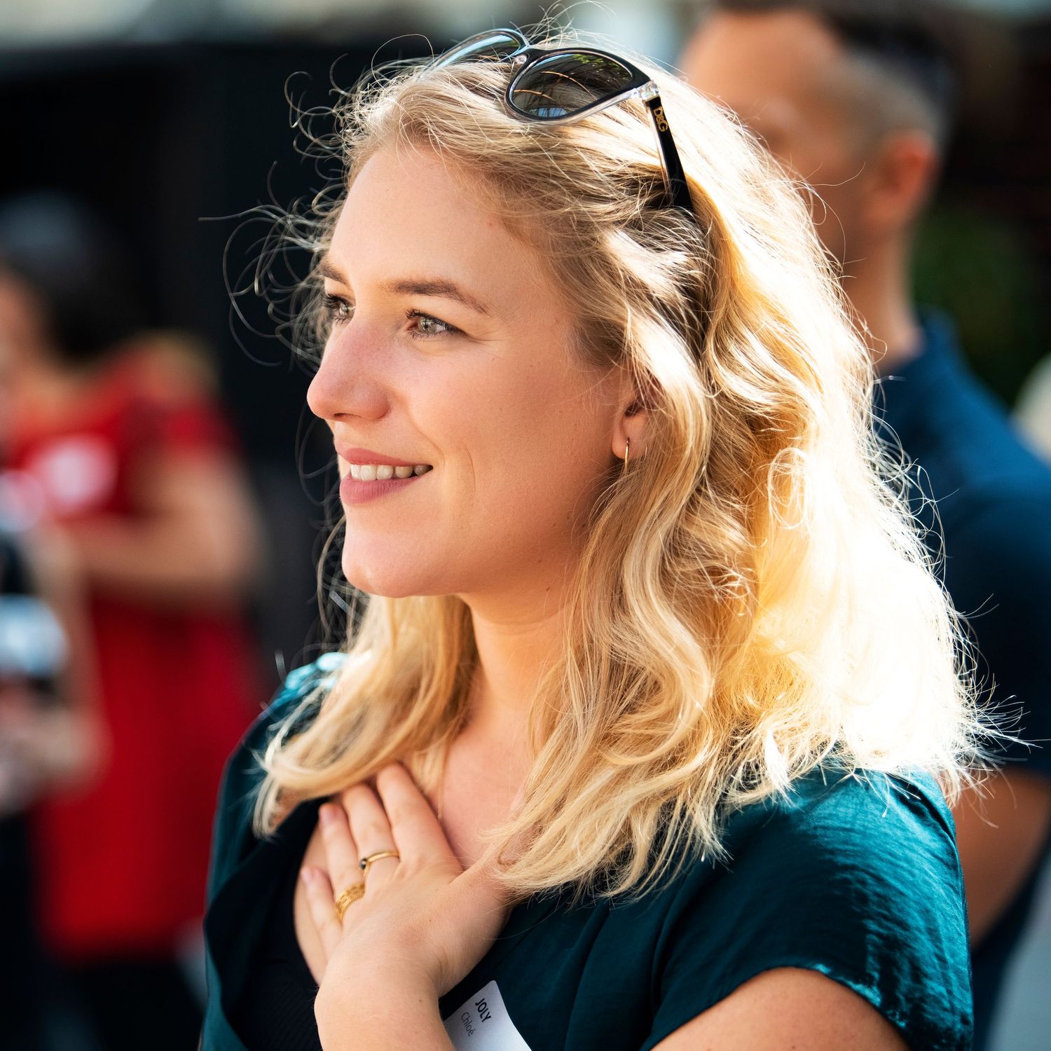 Sunlit portrait of a person with blonde hair smiling outdoors.