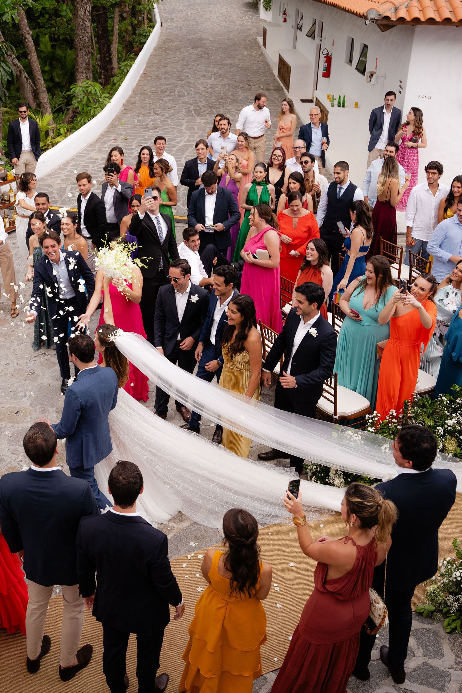 Wedding guests line up along a curved white wall during an outdoor celebration ceremony.