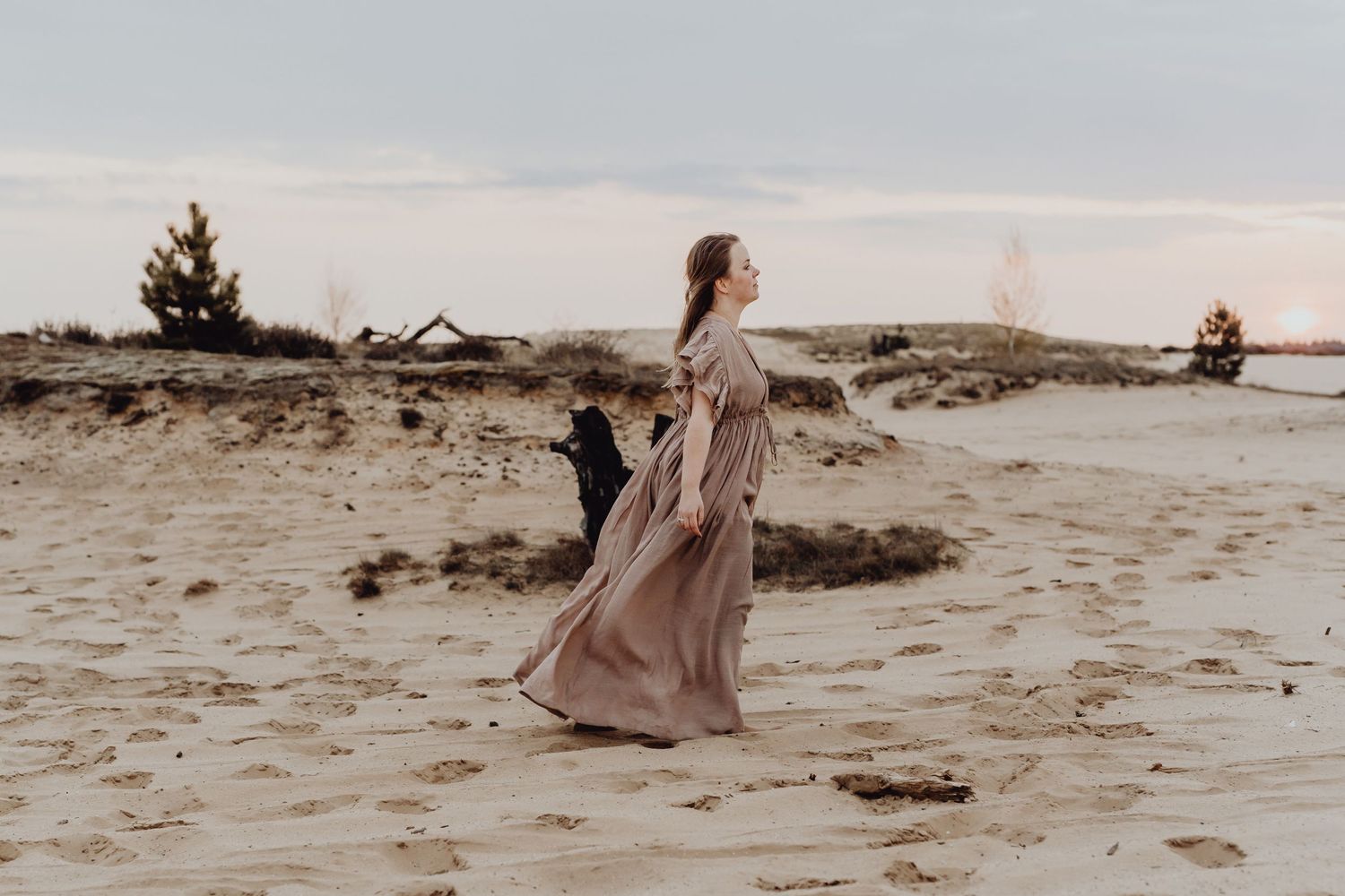 A person in a flowing dress walks with their dog along a sandy beach at dusk.