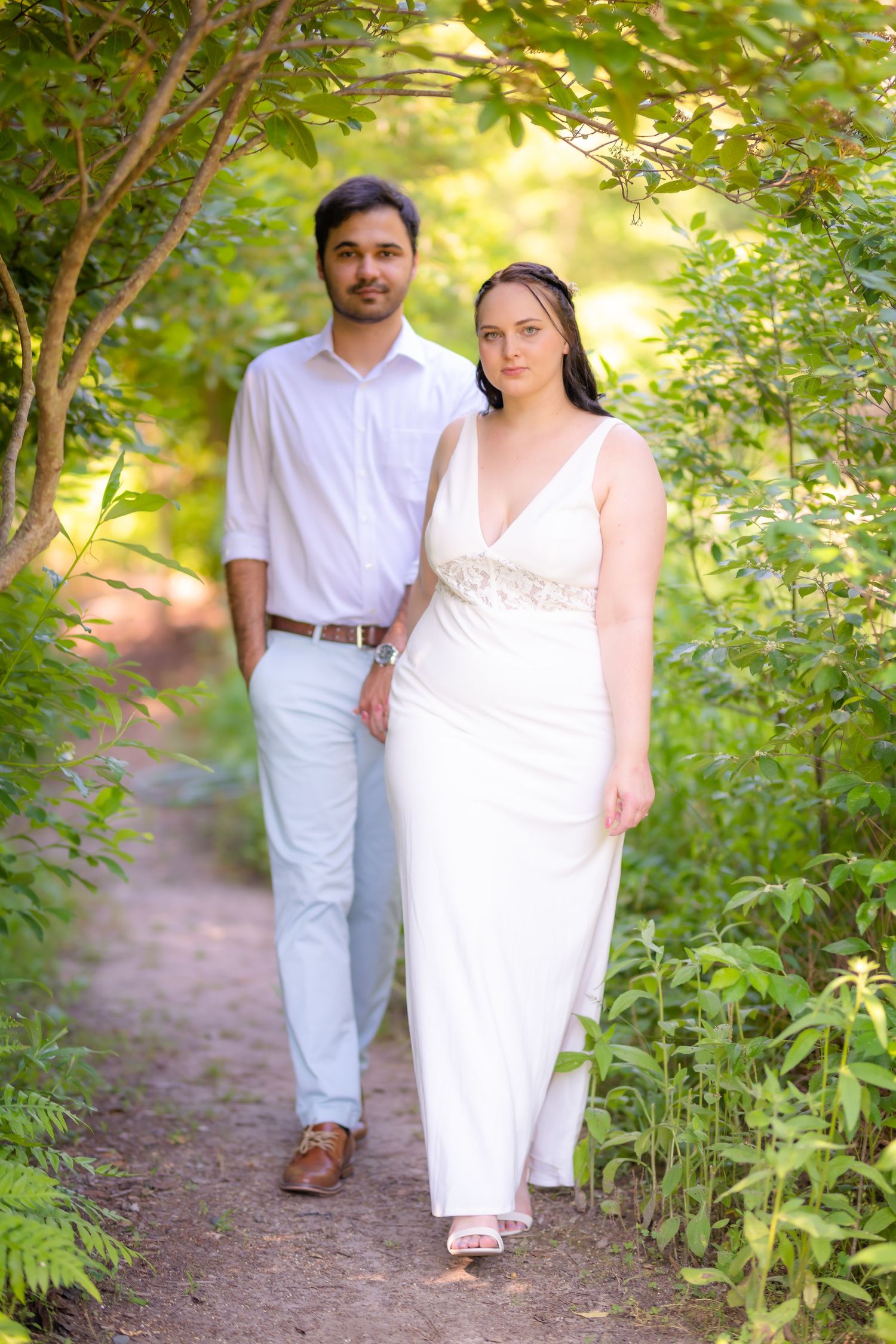 A couple poses together on a garden path surrounded by lush greenery.
