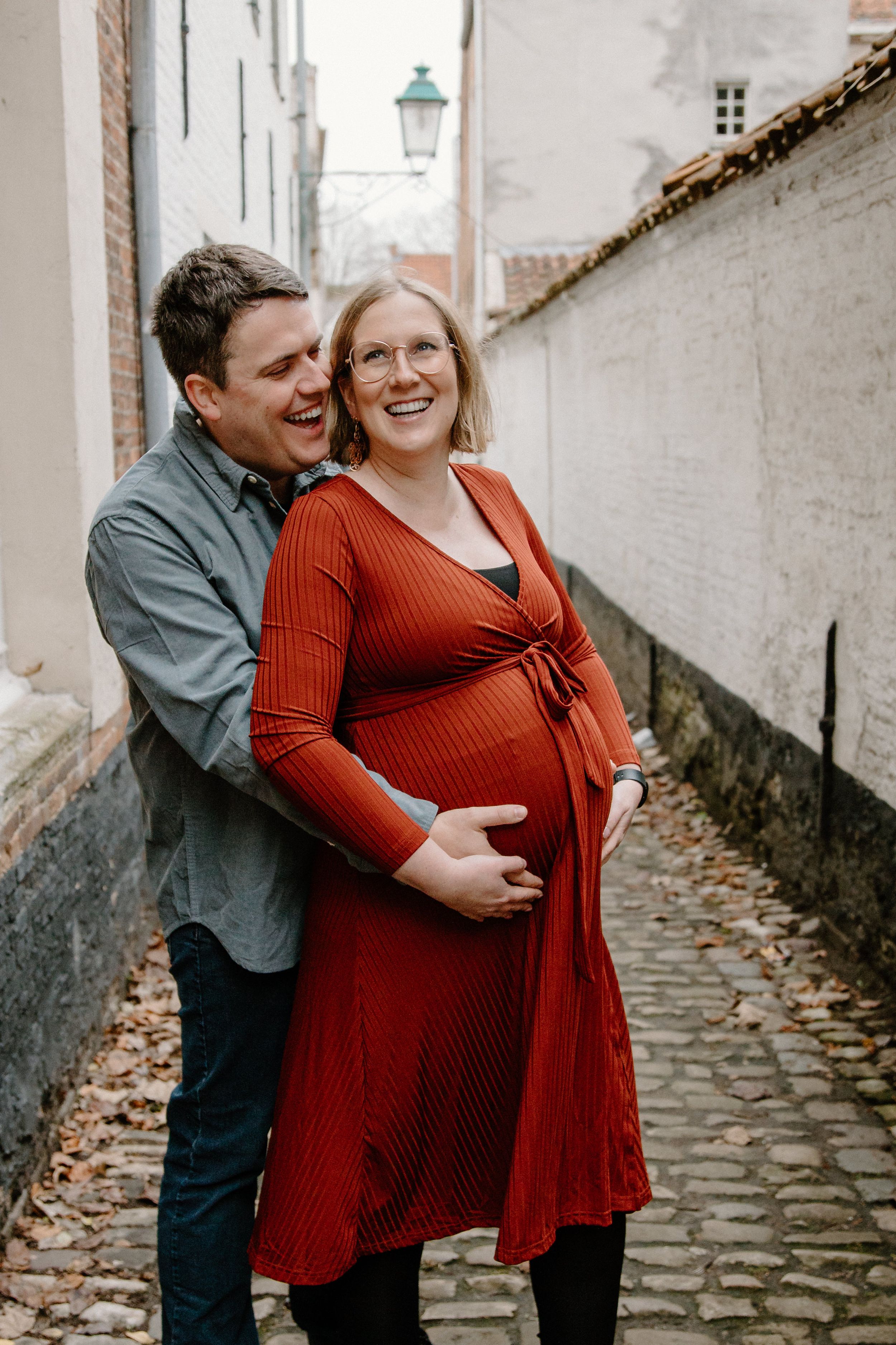 Couple sharing intimate moment on cobblestone street during maternity photoshoot.