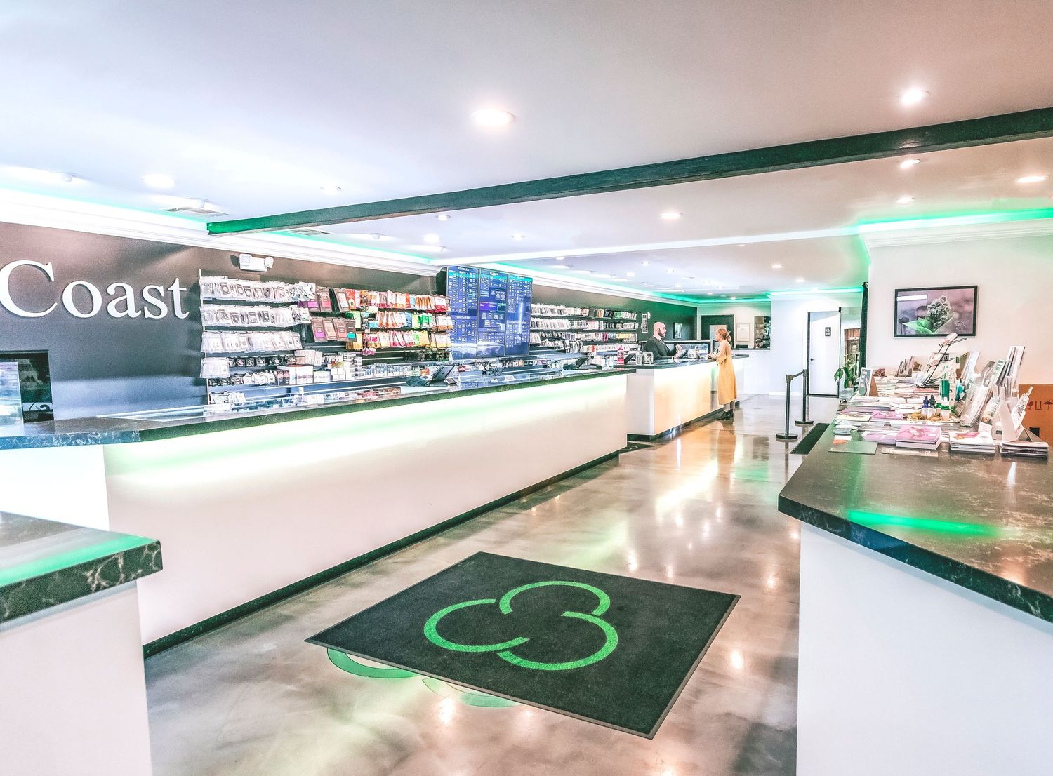 Modern Coast dispensary interior with green-lit display counters and merchandise shelving.