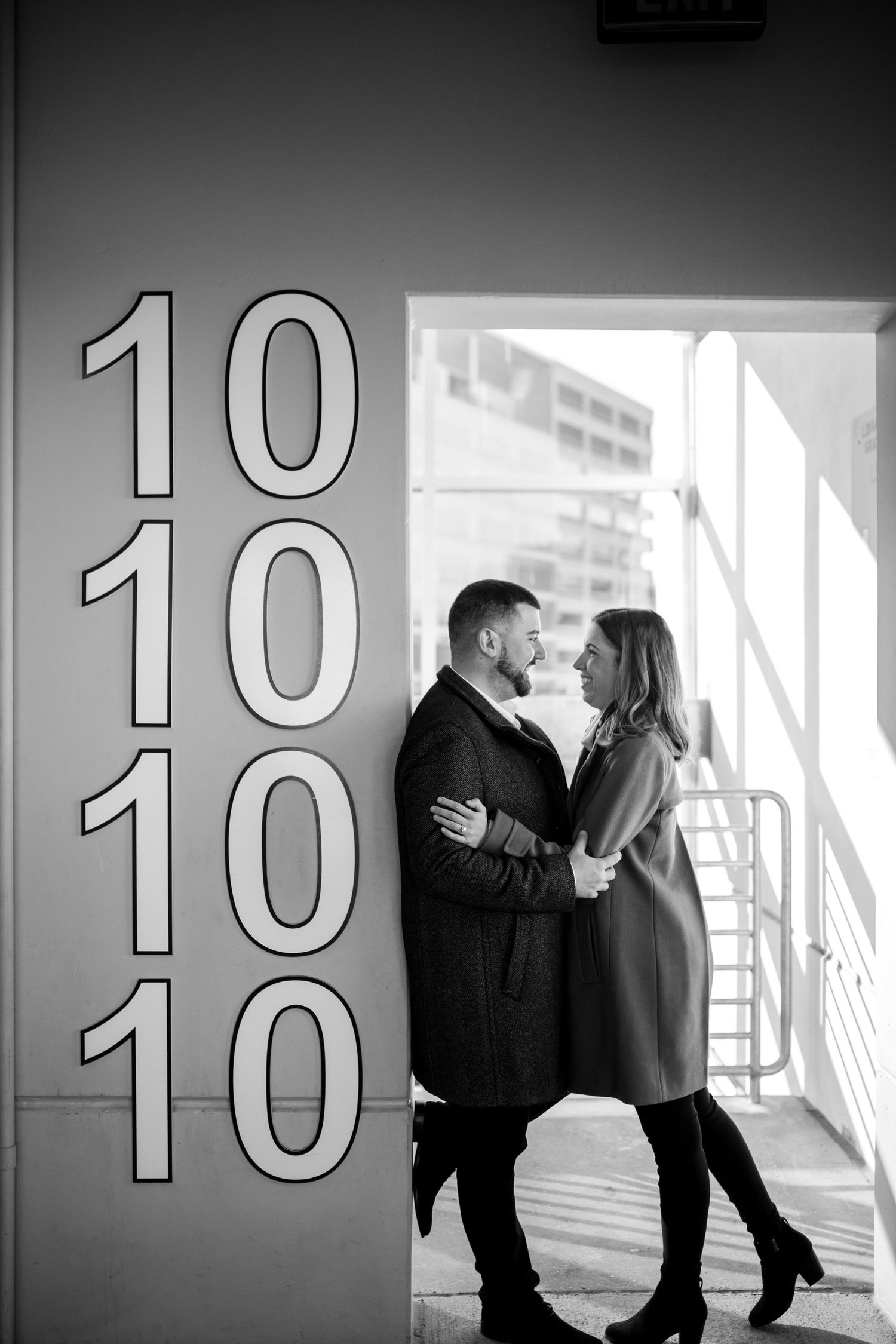 A romantic black and white photo showing a couple embracing near large numbers reading 10 10 10 10 on a wall.