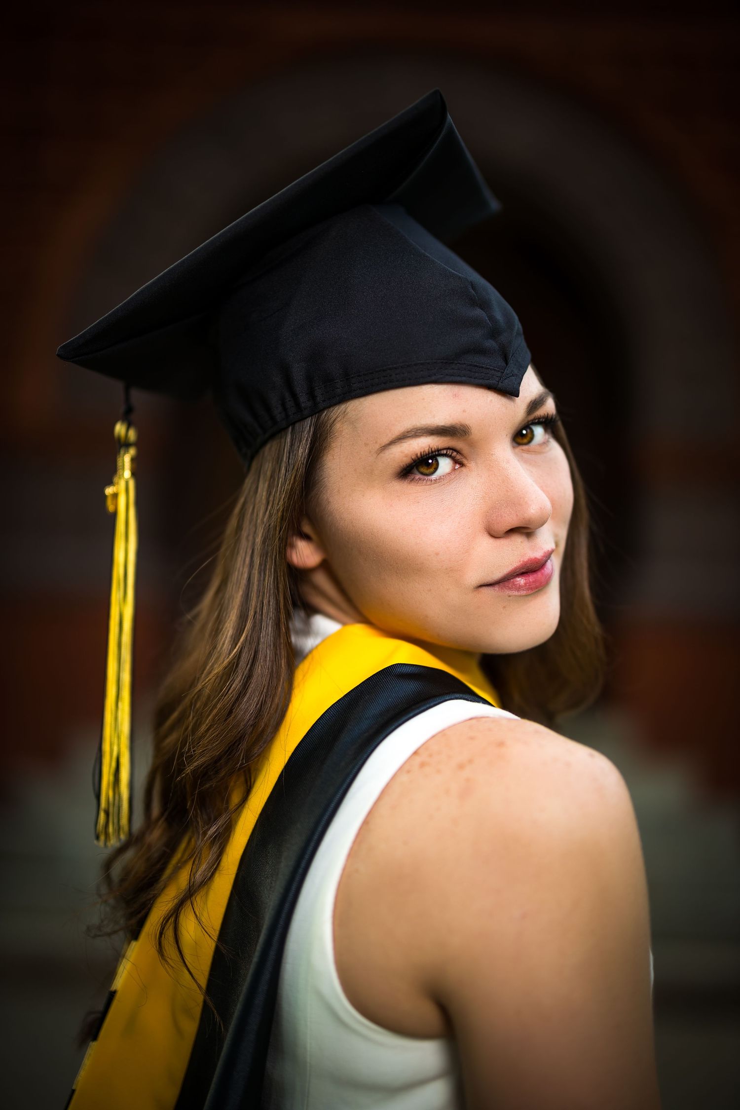 Graduate wearing yellow stole and black cap in profile against architectural backdrop.