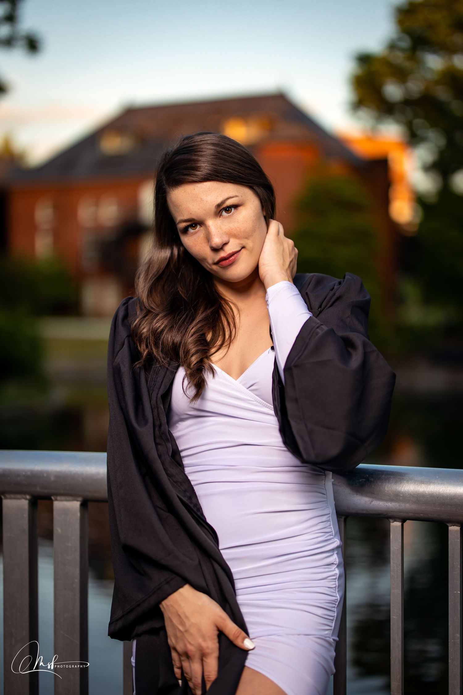Evening graduation portrait with black gown and white dress against brick building.
