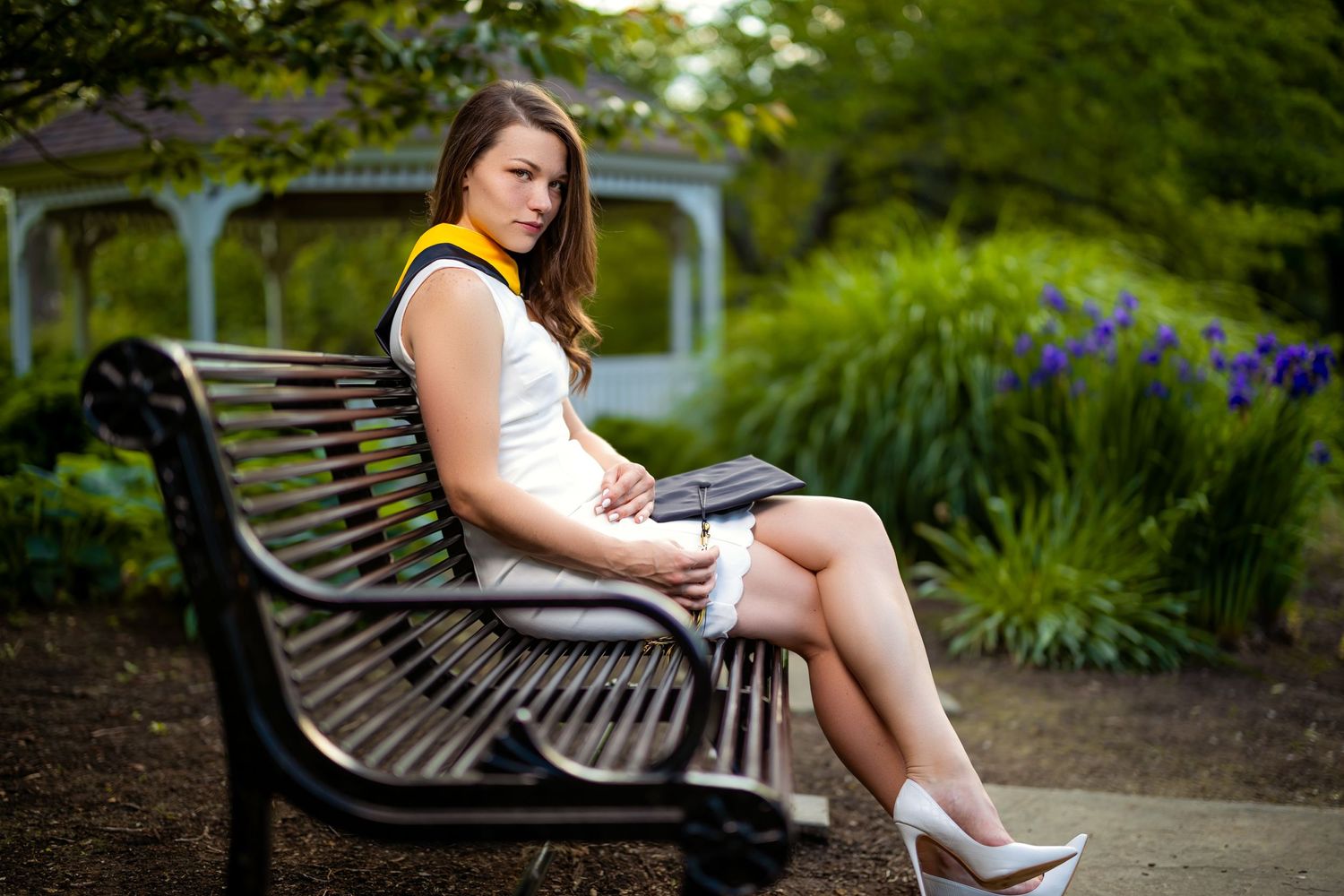 College graduation photo on park bench surrounded by gardens and gazebo.