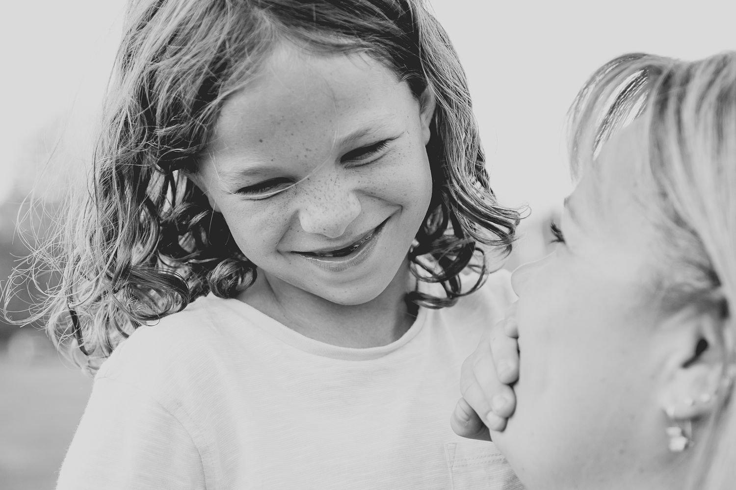 Black and white close-up of two children sharing a joyful moment together.