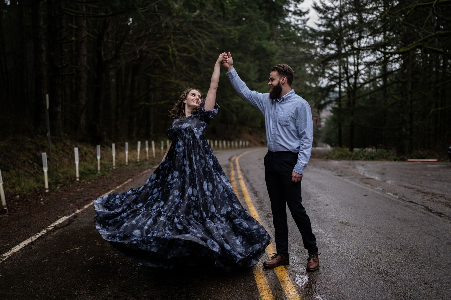 A couple dancing together on a wet forest road with a flowing dress.