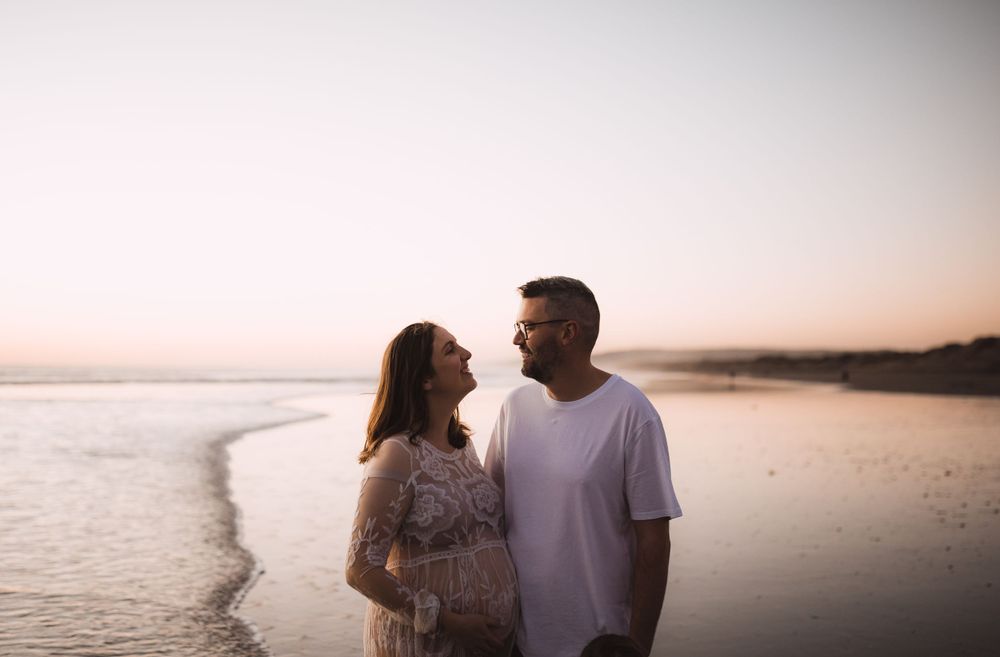 Couple sharing an intimate moment on beach at sunset with soft pink sky.