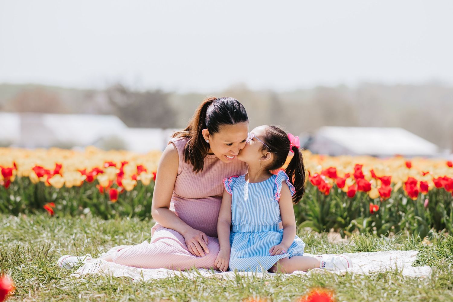 Two people share a tender moment while sitting on a blanket in a field of red tulips on a bright spring day.