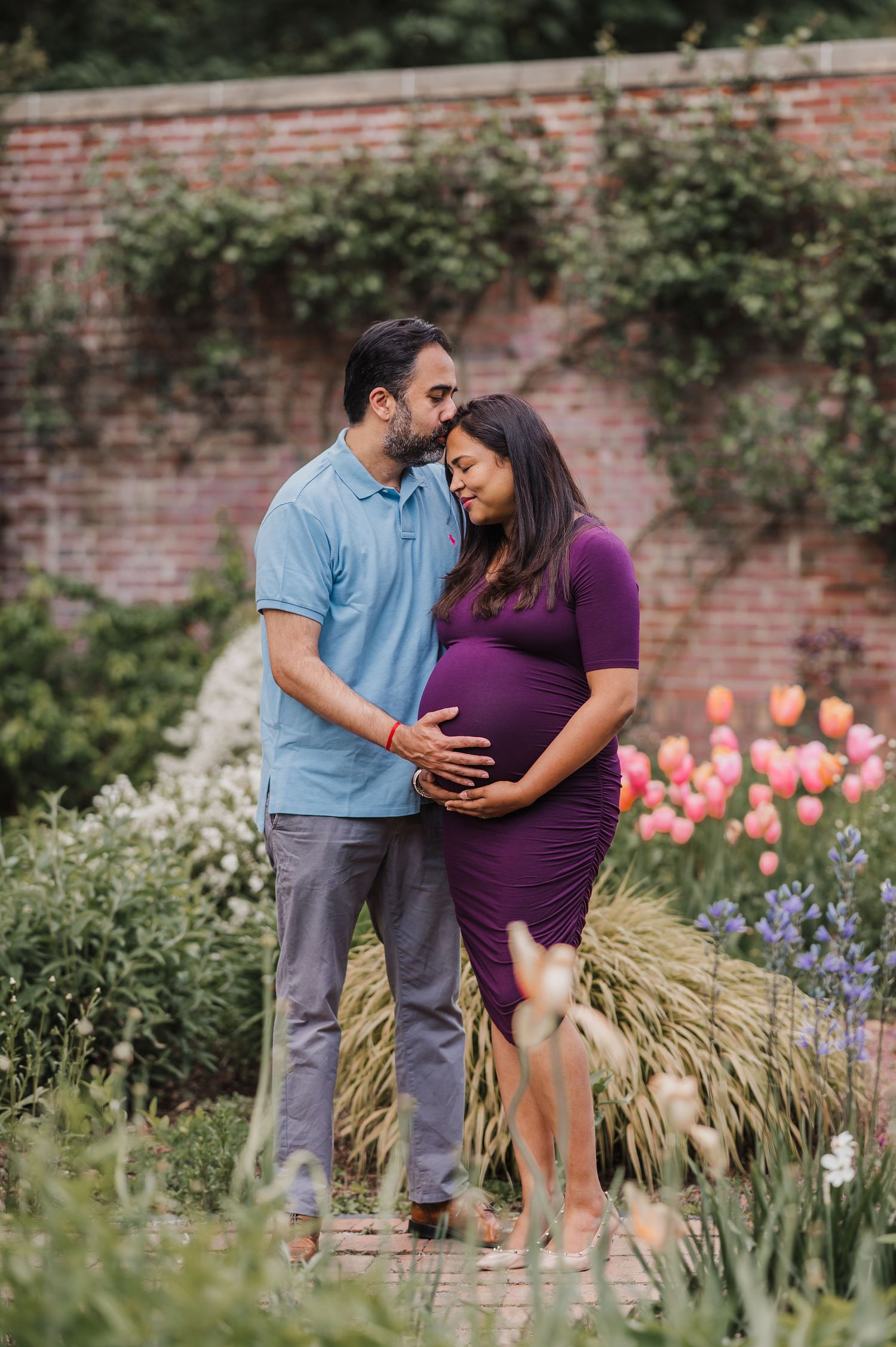 Couple sharing an intimate moment in a garden with blooming tulips and a rustic brick wall background.