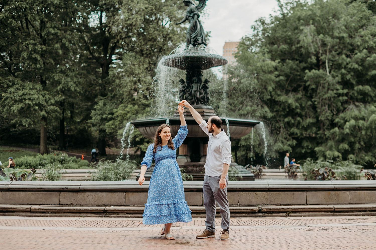 A couple dances joyfully in front of an ornate garden fountain on a summer afternoon in Central Park at Bethesda Terrace.