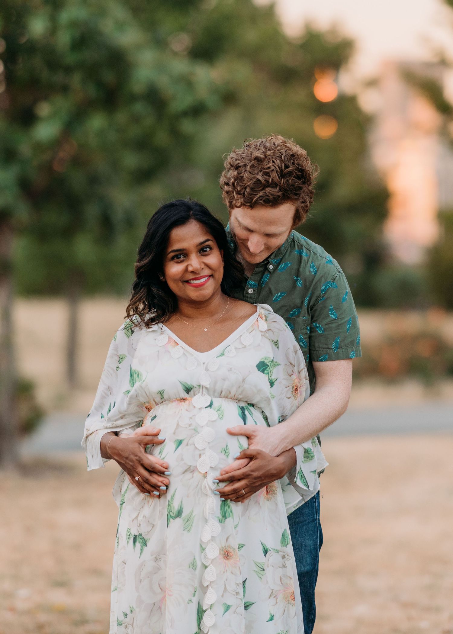 A couple embraces during a maternity photoshoot outdoors wearing floral and patterned outfits at sunset at Liberty State Park.