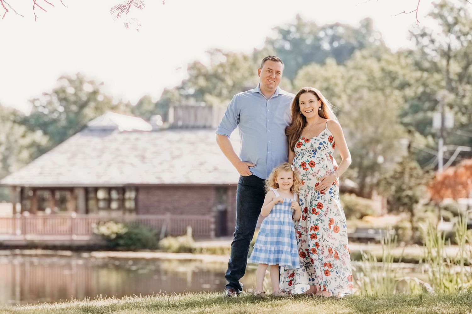A family stands together outdoors in summer attire with a rustic building and trees in the background at Verona Park.