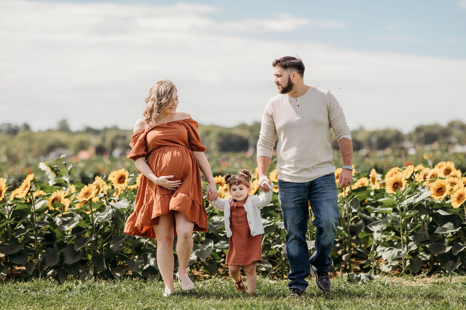 Family holding hands while walking together through a vibrant sunflower field on a sunny summer day at Holland Ridge Farms.