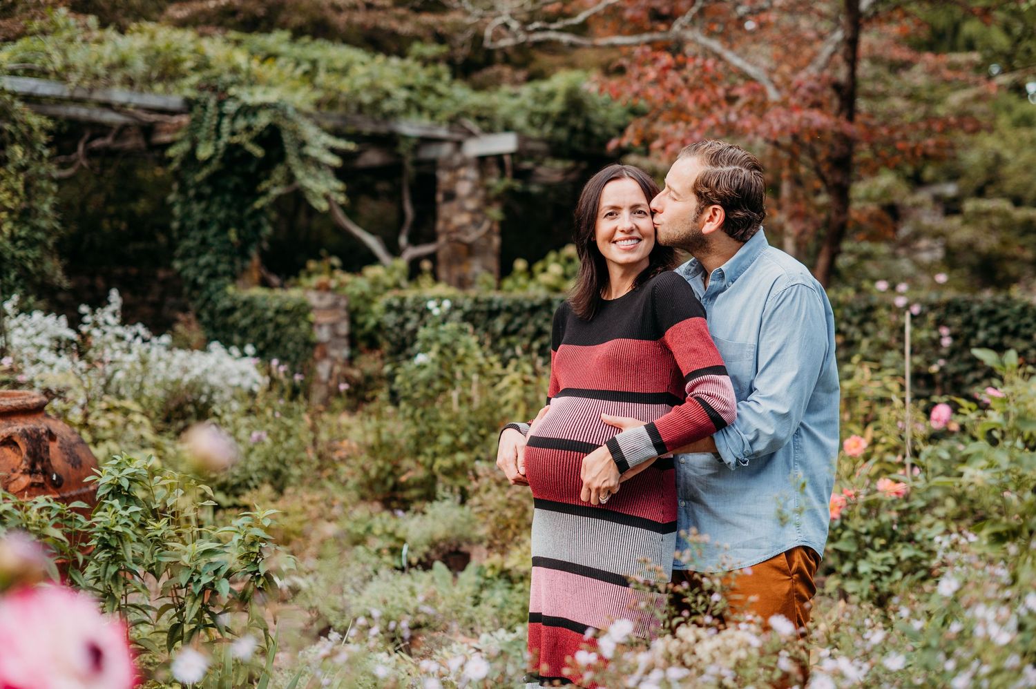 A loving couple shares an intimate moment while standing in a lush garden with autumn colors and blooming flowers in Morristown.