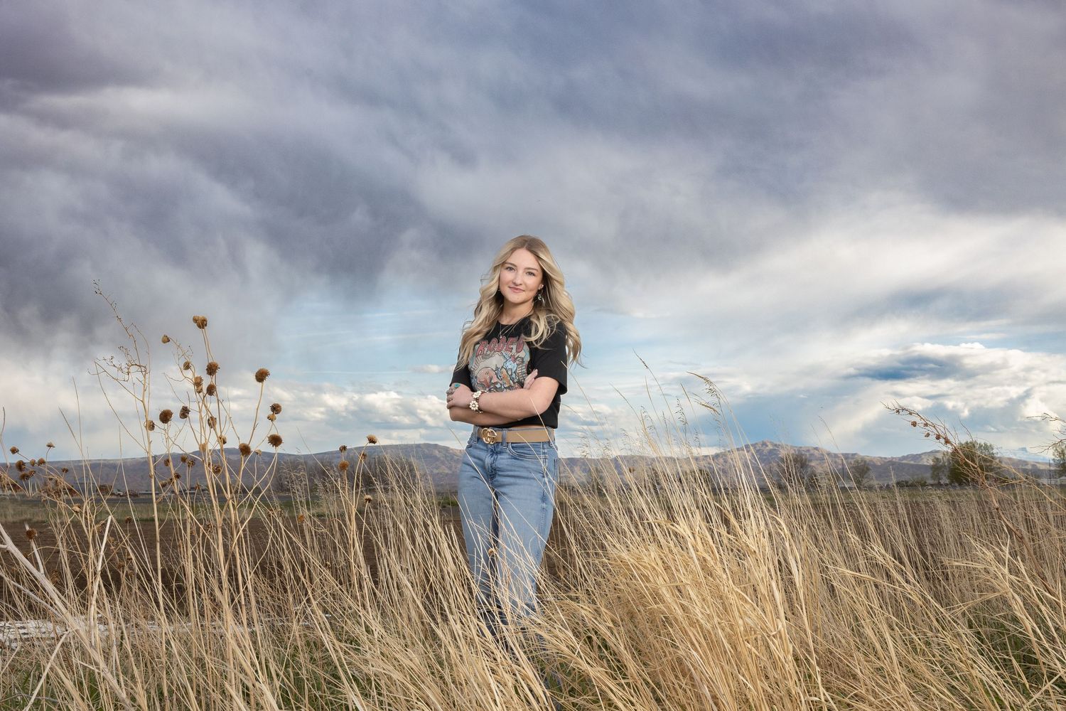 Natural portrait in tall grass with mountains and dramatic sky in background.