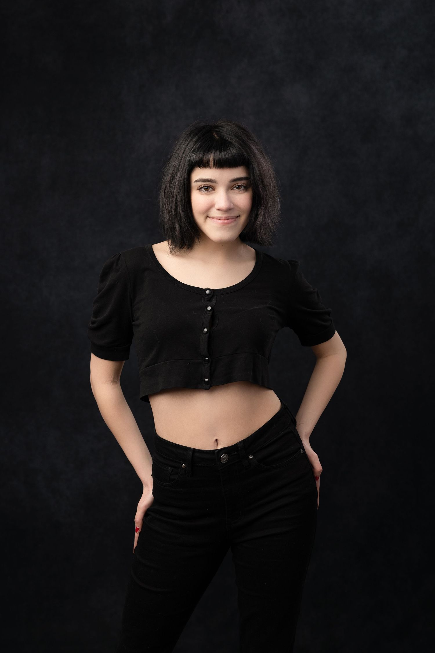 Studio fashion portrait featuring black crop top and high-waisted pants against dark background.