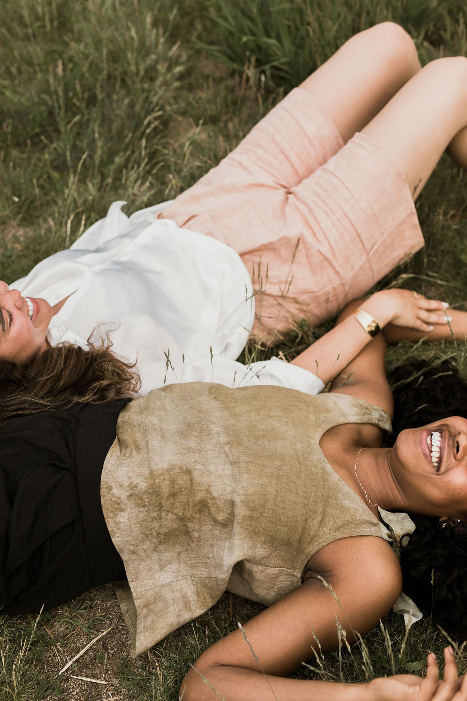 Two women laughing and lying in green grass on a sunny day.
