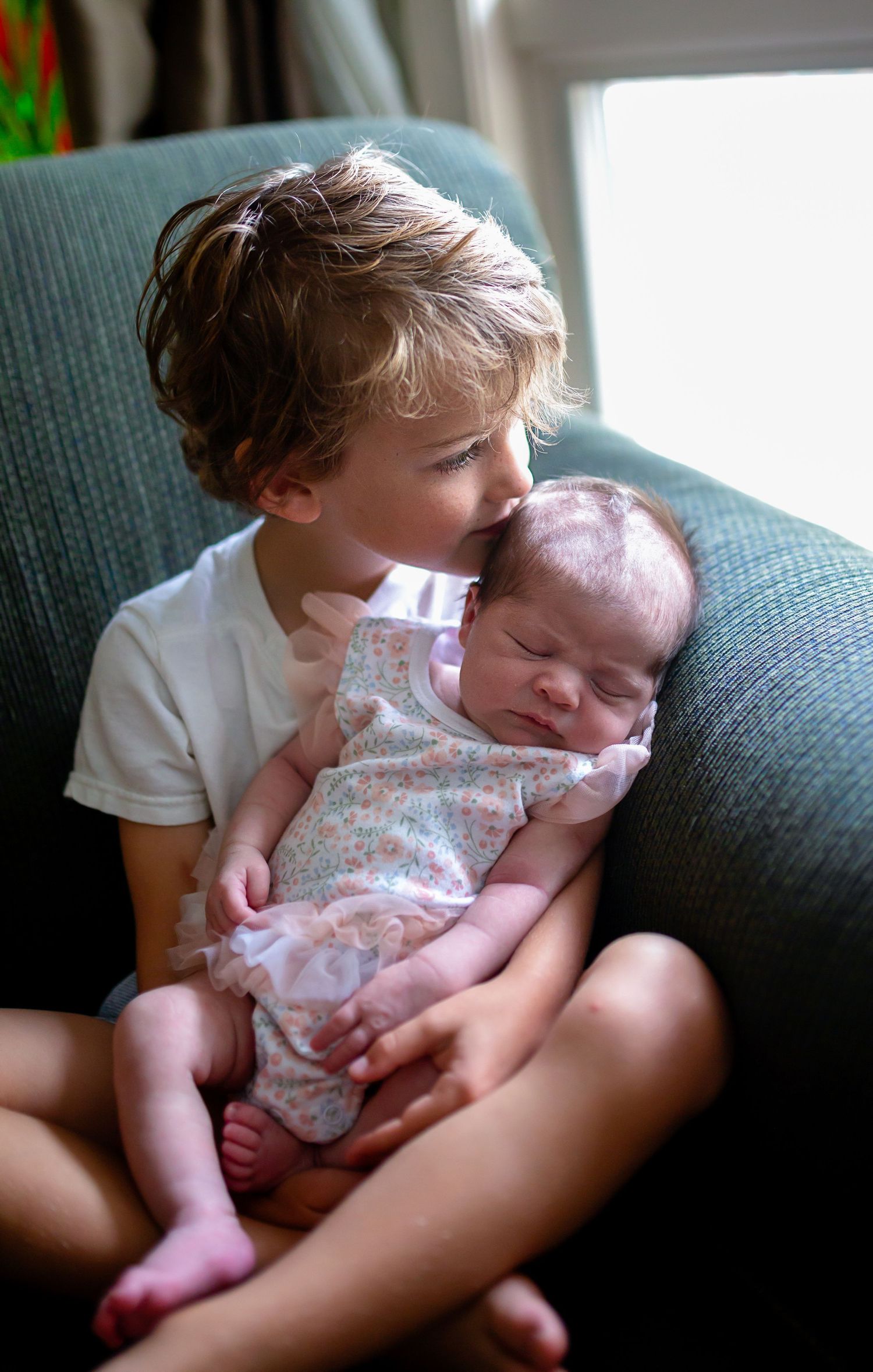 big brother holding his newborn baby sister while gazing out the window
