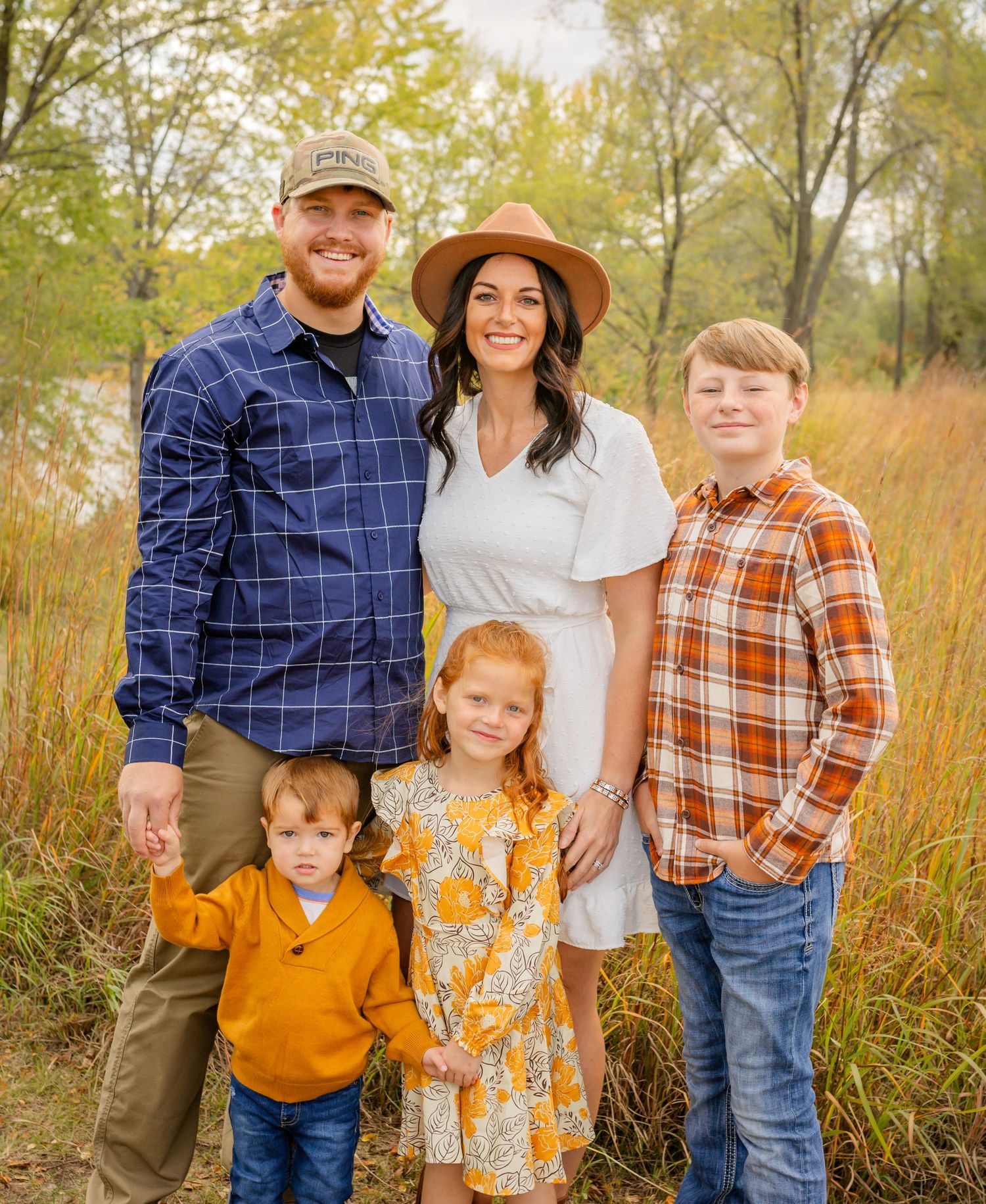 Family in coordinated fall colors poses together in tall prairie grass at sunset.