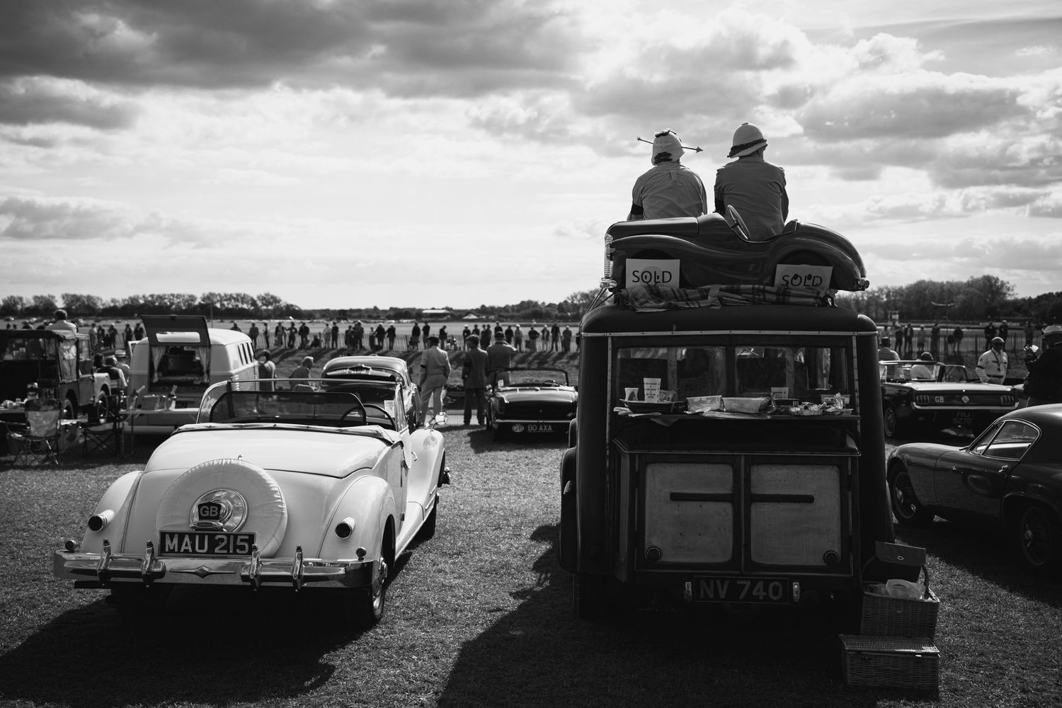 Vintage cars lined up at an outdoor classic car show under dramatic cloudy skies.