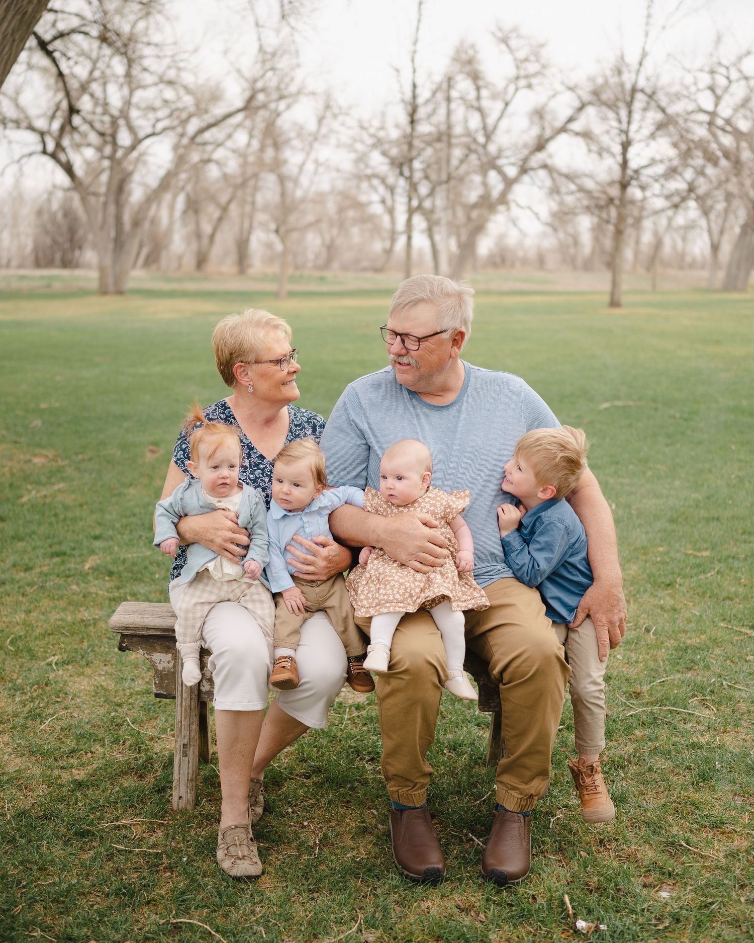 Multi-generational family sitting together on a wooden bench in a park setting.