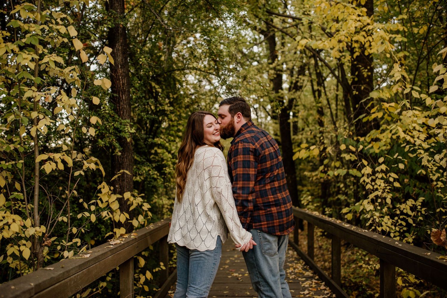 Couple embracing on wooden bridge surrounded by autumn foliage.